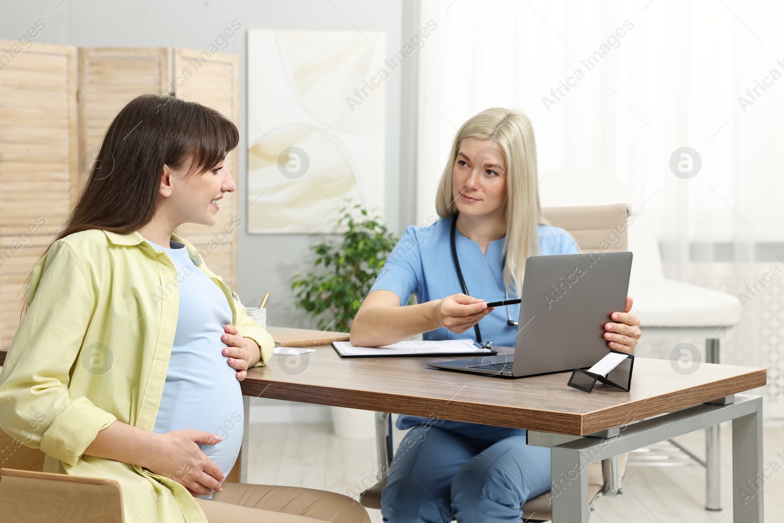 Photo of Doctor consulting pregnant patient at table in clinic