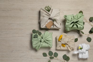 Photo of Furoshiki technique. Many gifts packed in fabric, flowers and eucalyptus leaves on wooden table, flat lay. Space for text