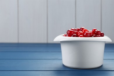 Photo of Fresh cranberries in bowl on blue wooden table, closeup. Space for text