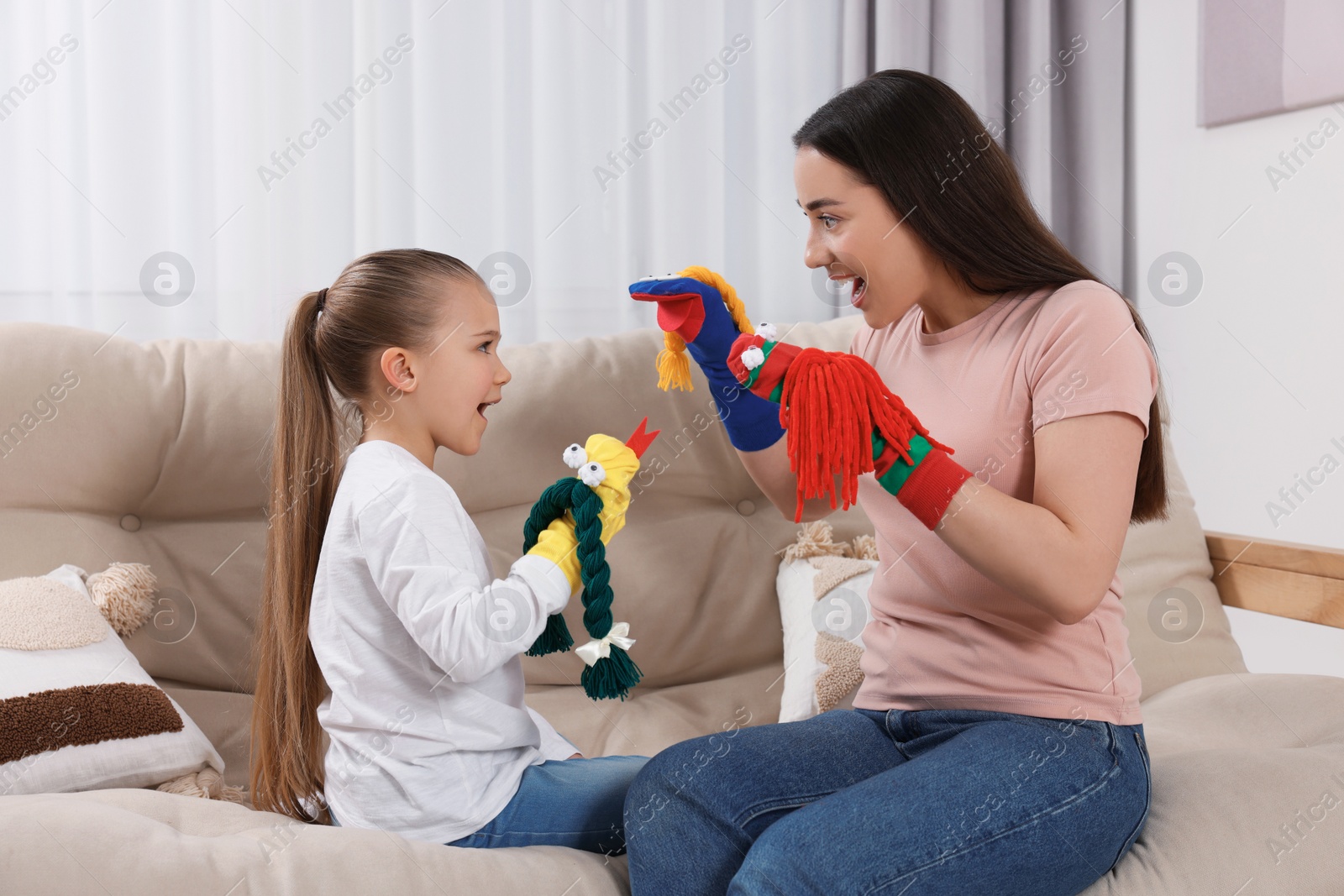 Photo of Emotional mother and daughter playing with funny sock puppets together at home