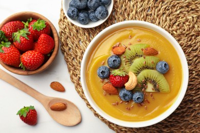 Photo of Delicious smoothie bowl with fresh berries, kiwi and nuts on white table, flat lay