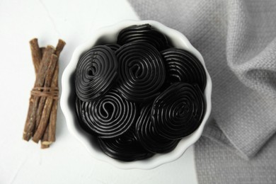 Photo of Tasty black candies and dried sticks of liquorice root on white table, flat lay