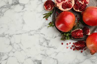 Photo of Delicious ripe pomegranates on white marble table, flat lay. Space for text