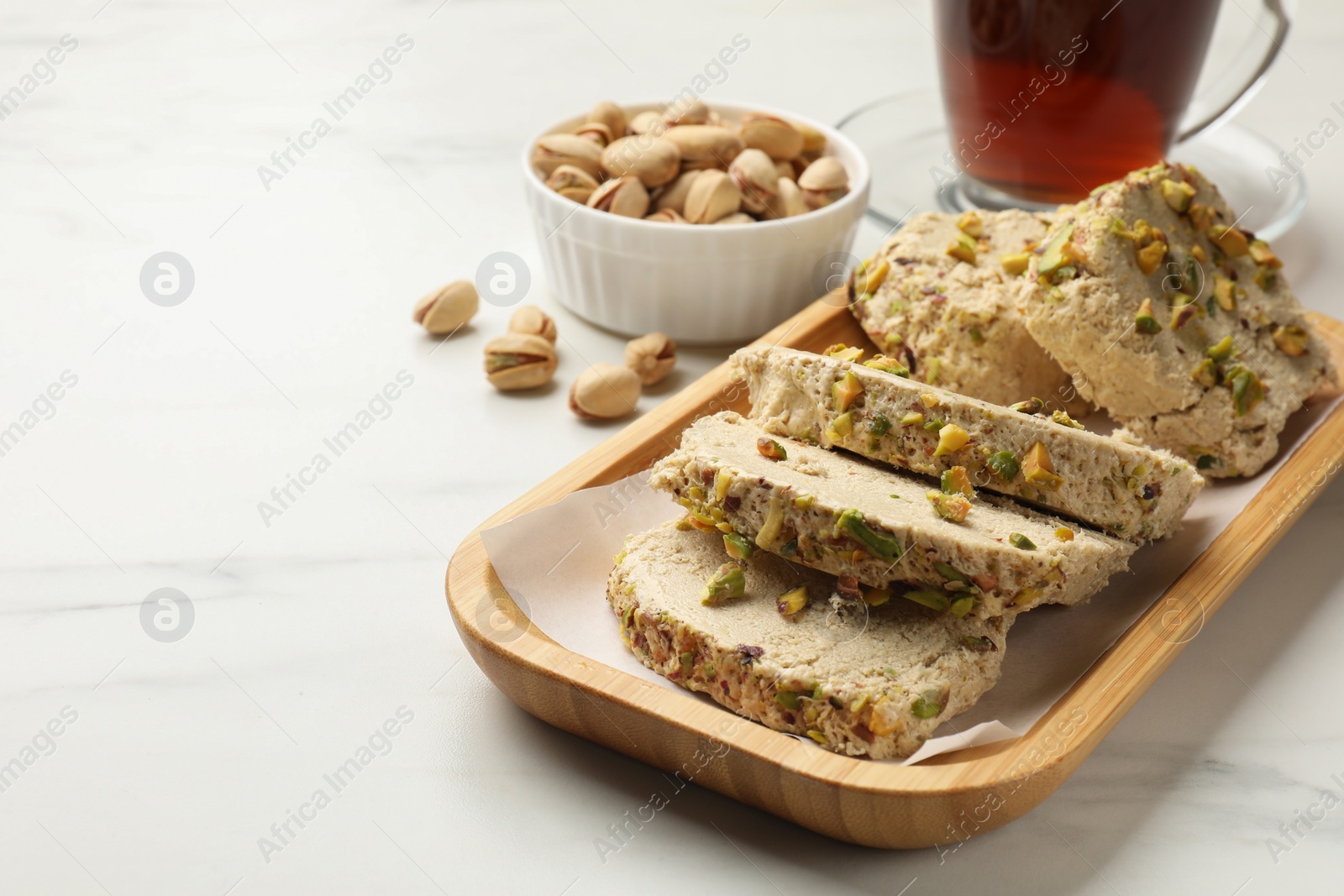 Photo of Tasty halva with pistachios served on white marble table, closeup. Space for text