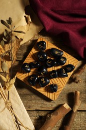 Photo of Composition with black rune stones and dried plants on wooden table, flat lay