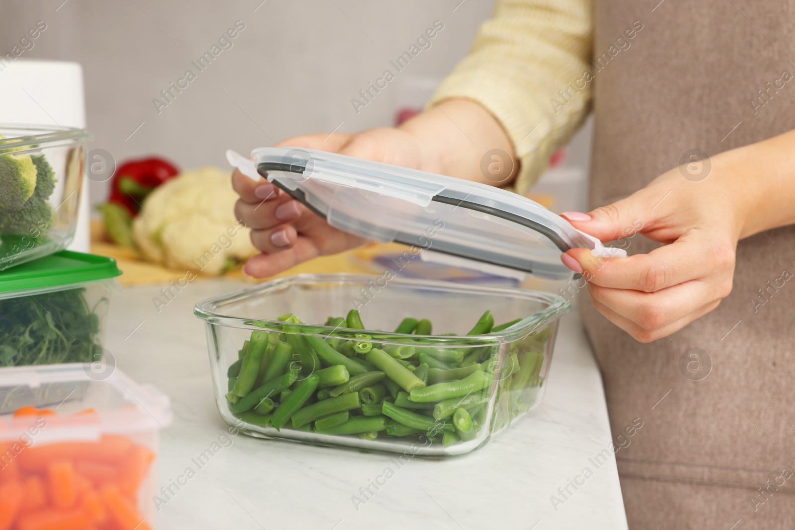Photo of Woman sealing glass container with lid at white marble table in kitchen, closeup. Food storage