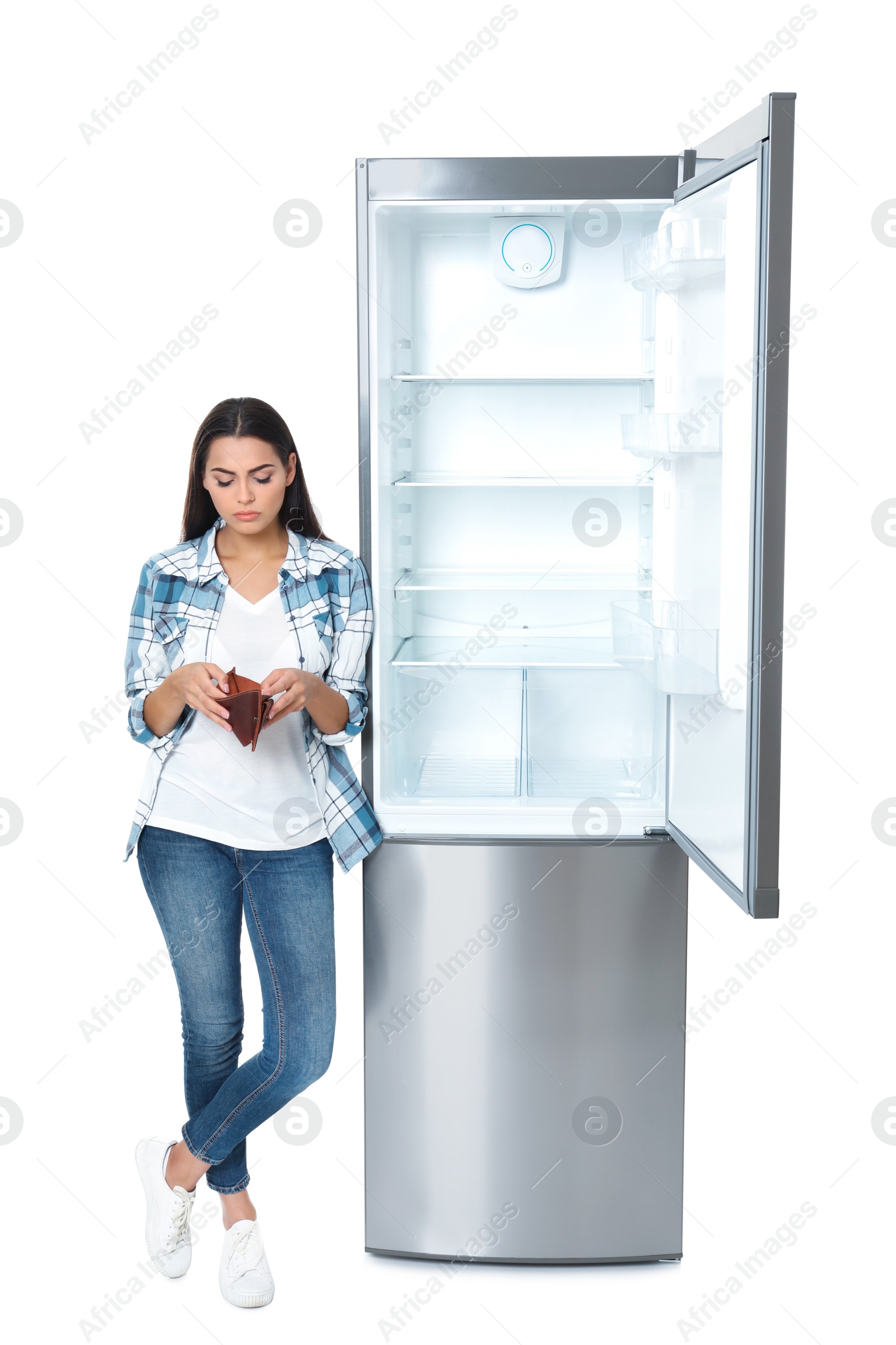 Photo of Young woman with no money in wallet near empty refrigerator on white background