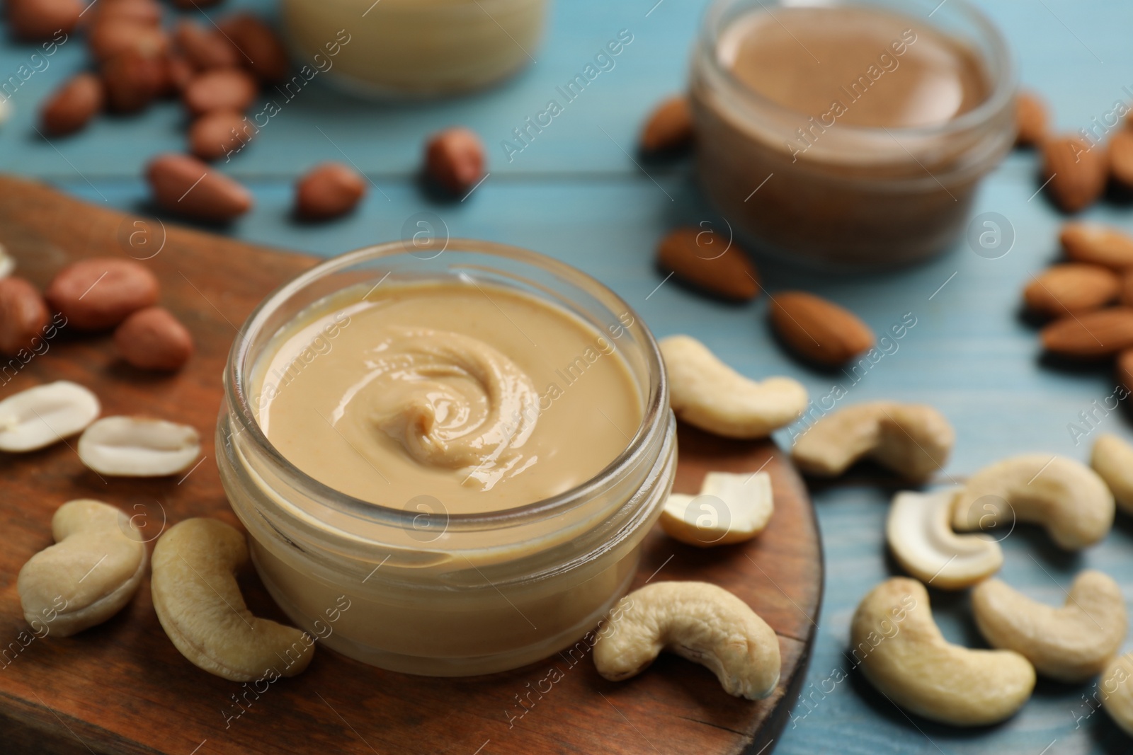 Photo of Jars with butters made of different nuts and ingredients on light blue wooden table, closeup