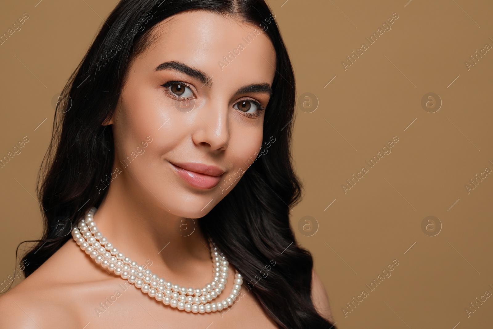 Photo of Young woman wearing elegant pearl necklace on brown background, space for text