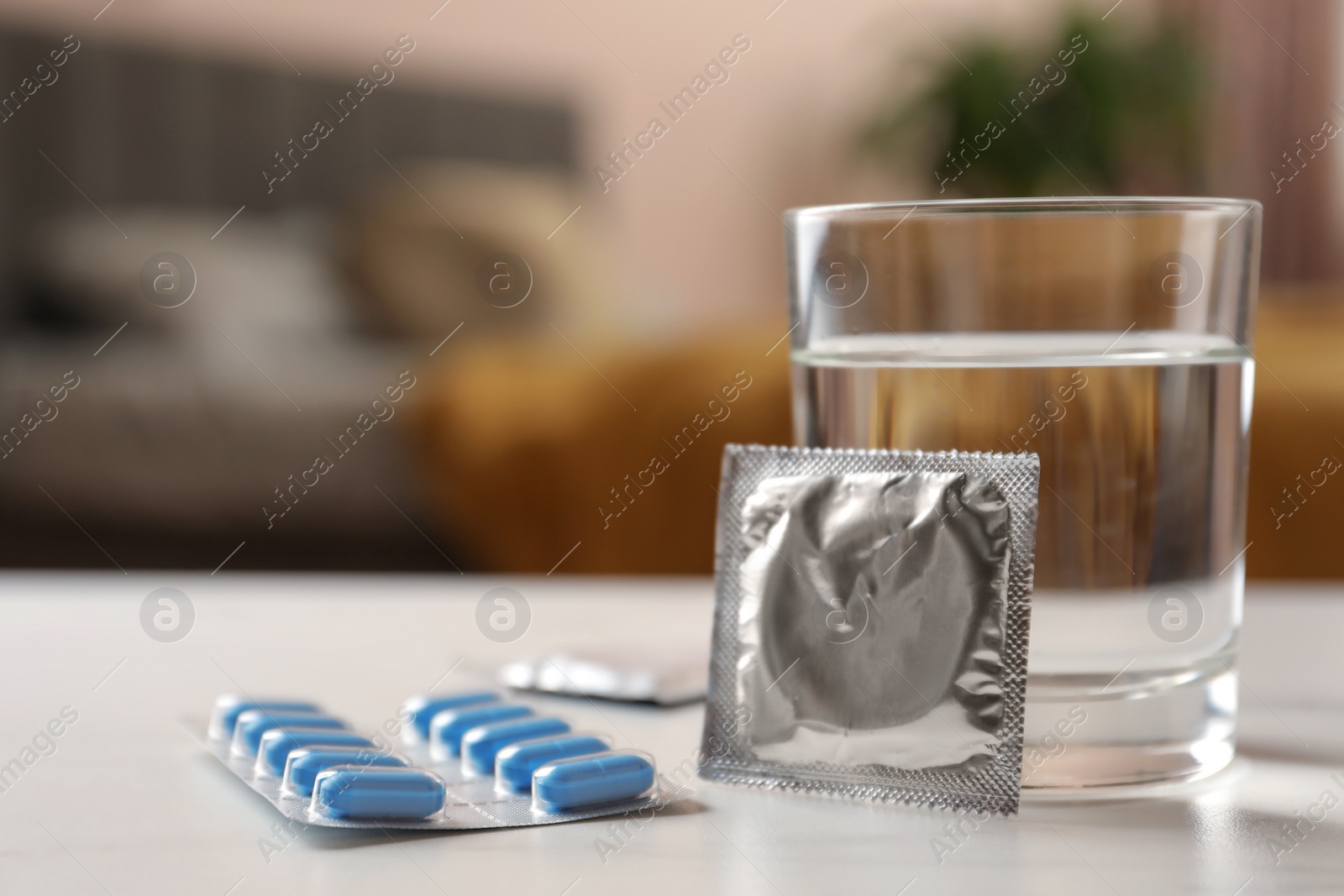 Photo of Glass of water, condoms and pills on white table indoors, closeup with space for text. Potency problem concept