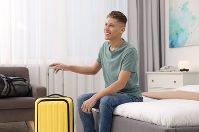 Photo of Smiling guest with suitcase relaxing on bed in stylish hotel room