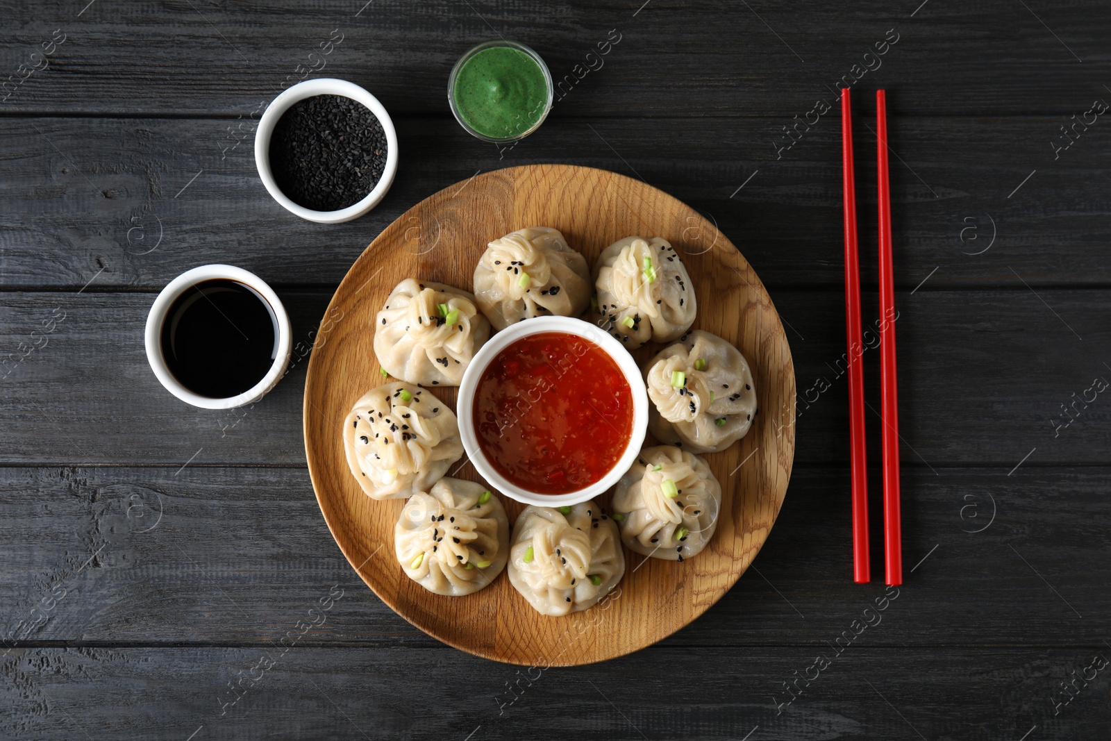 Photo of Flat lay composition with plate of tasty baozi dumplings, sesame seeds and sauces on wooden table