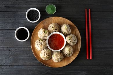 Photo of Flat lay composition with plate of tasty baozi dumplings, sesame seeds and sauces on wooden table