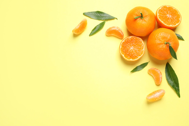 Photo of Flat lay composition with fresh ripe tangerines and leaves on light yellow background, space for text. Citrus fruit