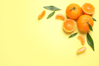 Flat lay composition with fresh ripe tangerines and leaves on light yellow background, space for text. Citrus fruit