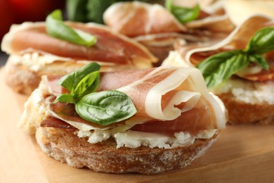 Photo of Tasty sandwiches with cured ham and basil on wooden board, closeup