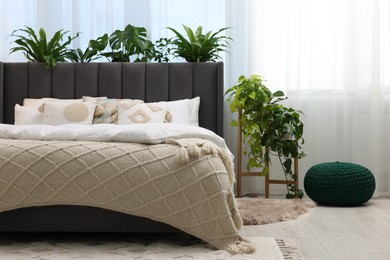 Photo of Comfortable bed, pouf and beautiful houseplants in bedroom. Interior design