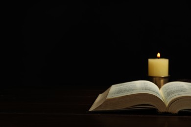 Photo of Church candle and Bible on wooden table against black background, space for text