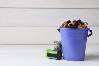Image of Many different used electric batteries in bucket on white wooden table. Space for text