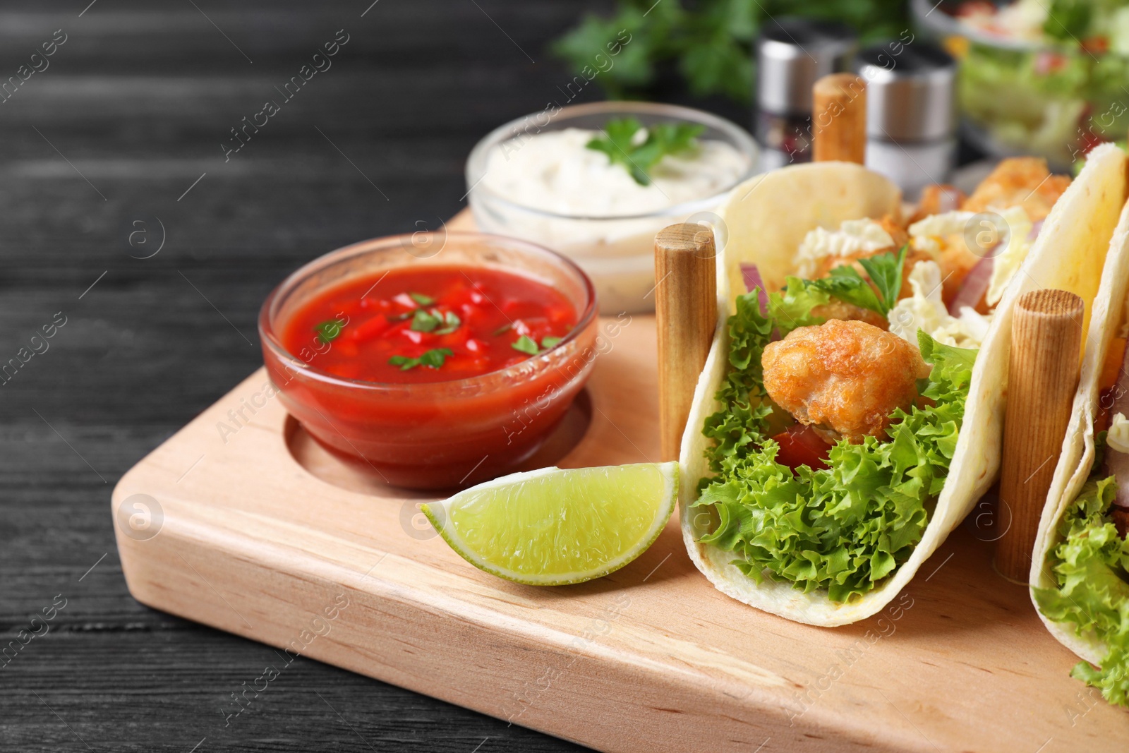 Photo of Delicious fish tacos served on dark wooden table, closeup