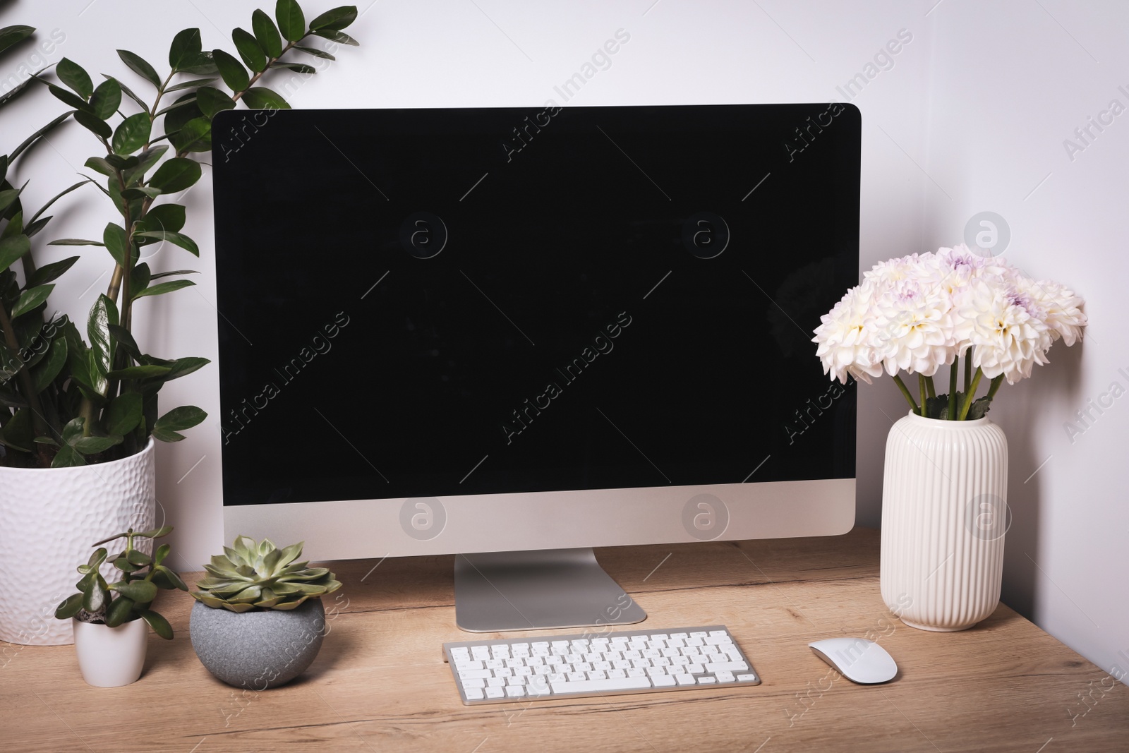 Photo of Comfortable workplace with modern computer, green houseplants and beautiful flowers on wooden table indoors