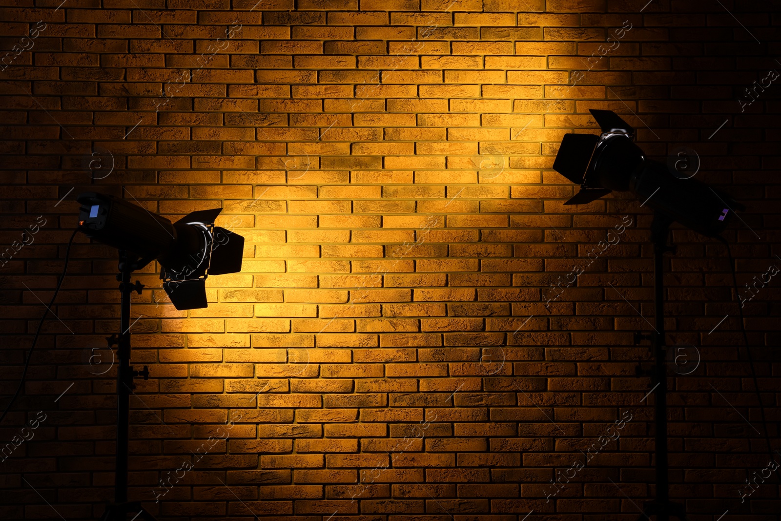 Photo of Bright yellow spotlights near brick wall in dark room, space for text