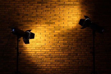 Photo of Bright yellow spotlights near brick wall in dark room, space for text
