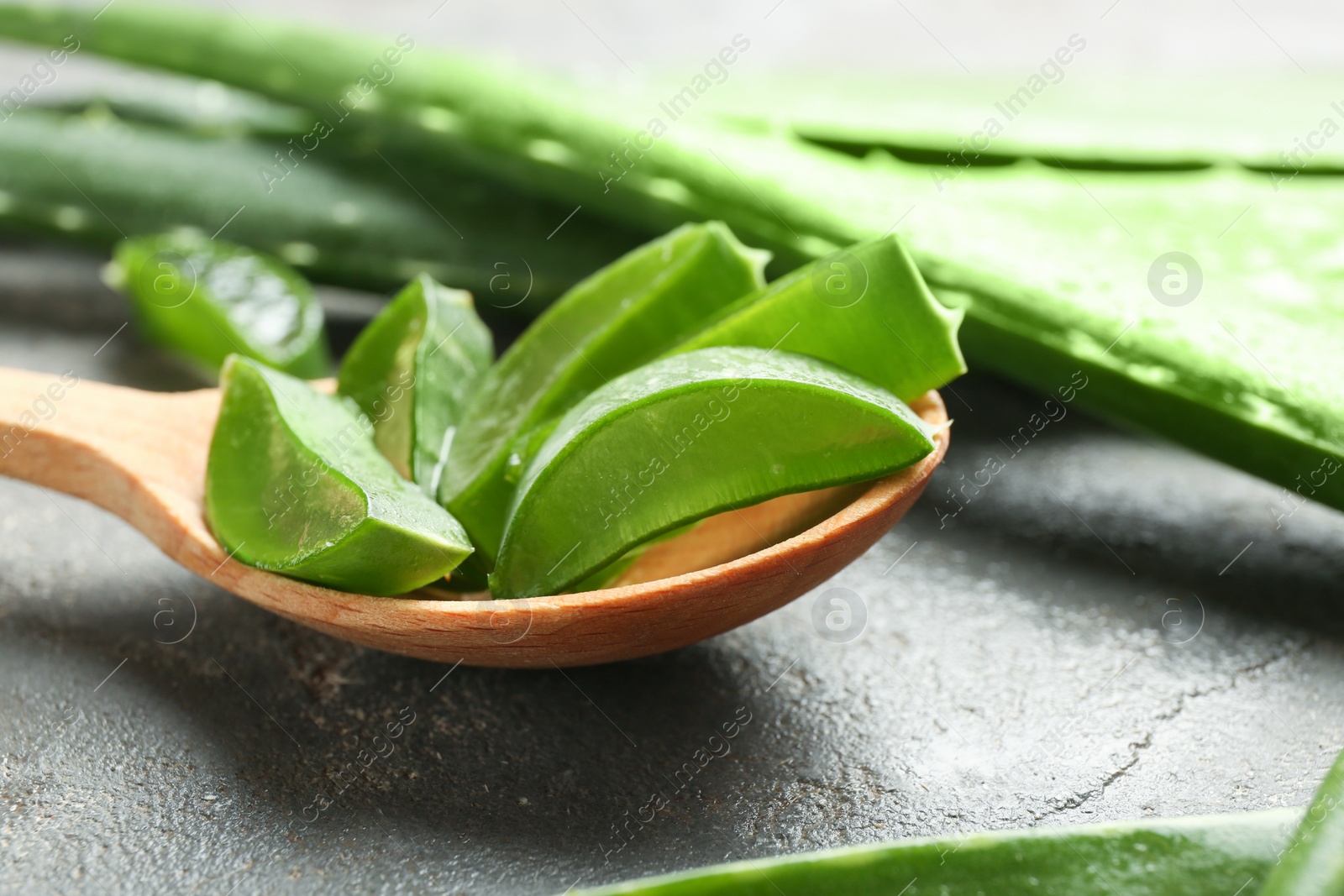 Photo of Wooden spoon and fresh aloe vera leaves on gray table