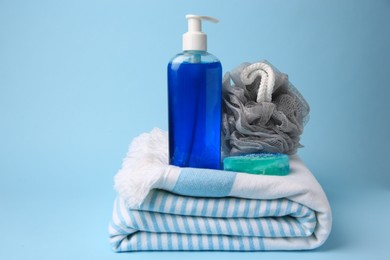 Grey shower puff, cosmetic products and towel on light blue background