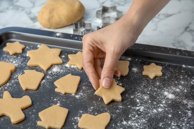 Photo of Young woman putting raw Christmas cookies on baking tray