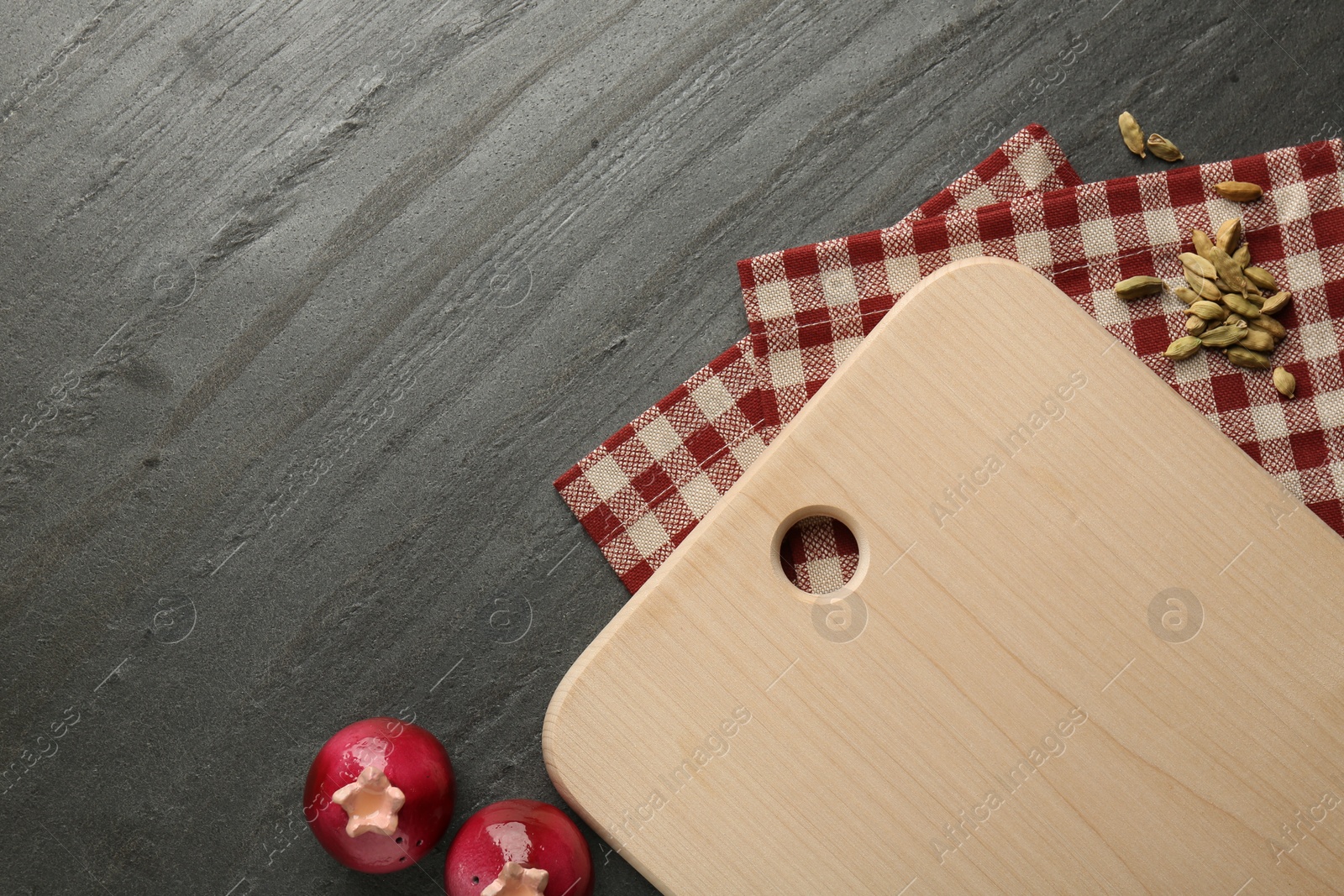 Photo of Wooden cutting board, kitchen towel and cardamom pods on dark grey table, flat lay. Space for text