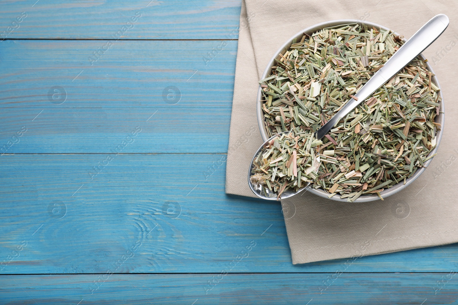 Photo of Bowl with aromatic dried lemongrass and spoon on light blue wooden table, flat lay. Space for text