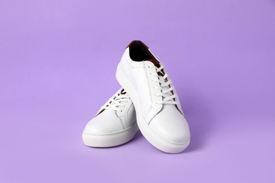 Pair of stylish white sneakers on violet background