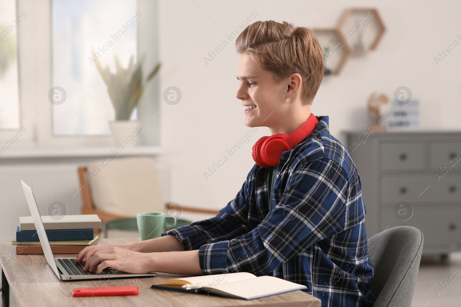 Photo of Online learning. Smiling teenage boy typing on laptop at home