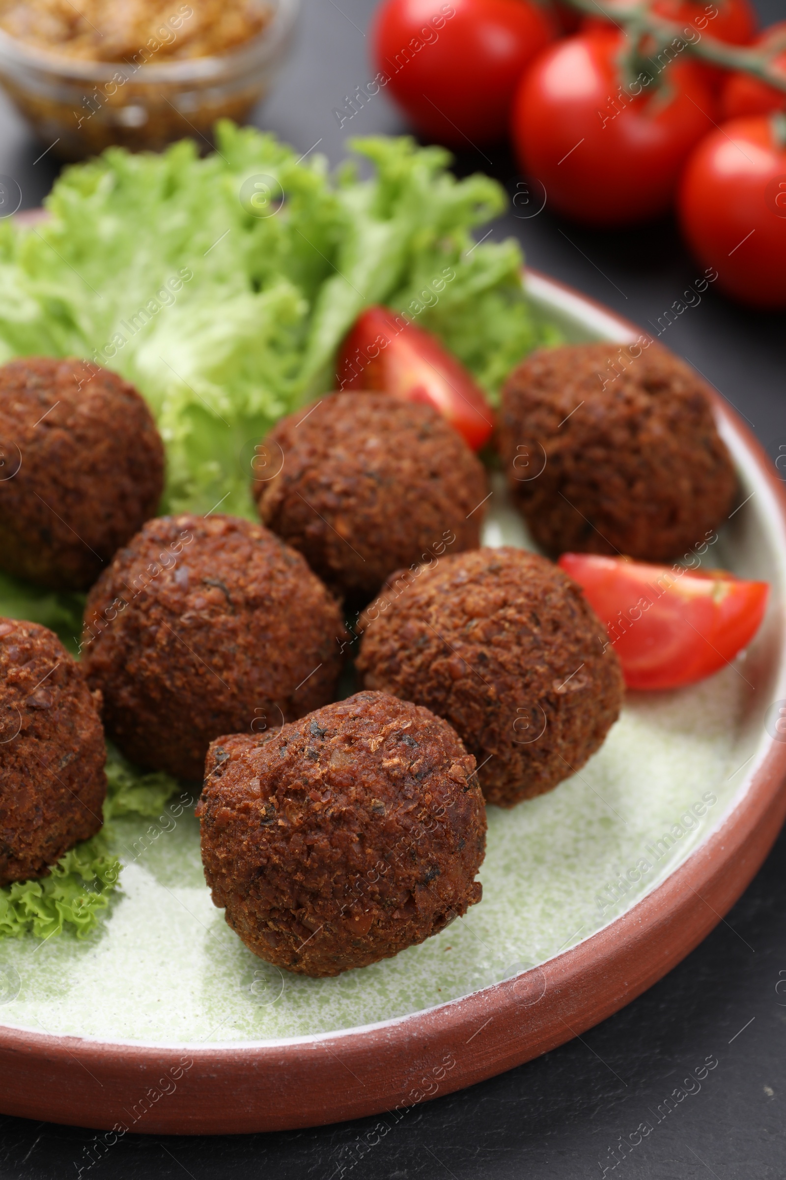 Photo of Delicious falafel balls, tomatoes and lettuce on dark table, closeup. Vegan meat products