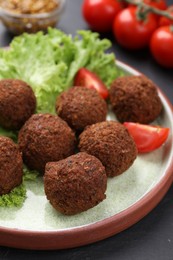 Delicious falafel balls, tomatoes and lettuce on dark table, closeup. Vegan meat products