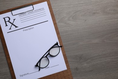 Photo of Clipboard with medical prescription form and glasses on wooden table, top view. Space for text