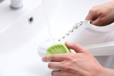 Photo of Woman washing stylish sneakers with brush in sink, closeup