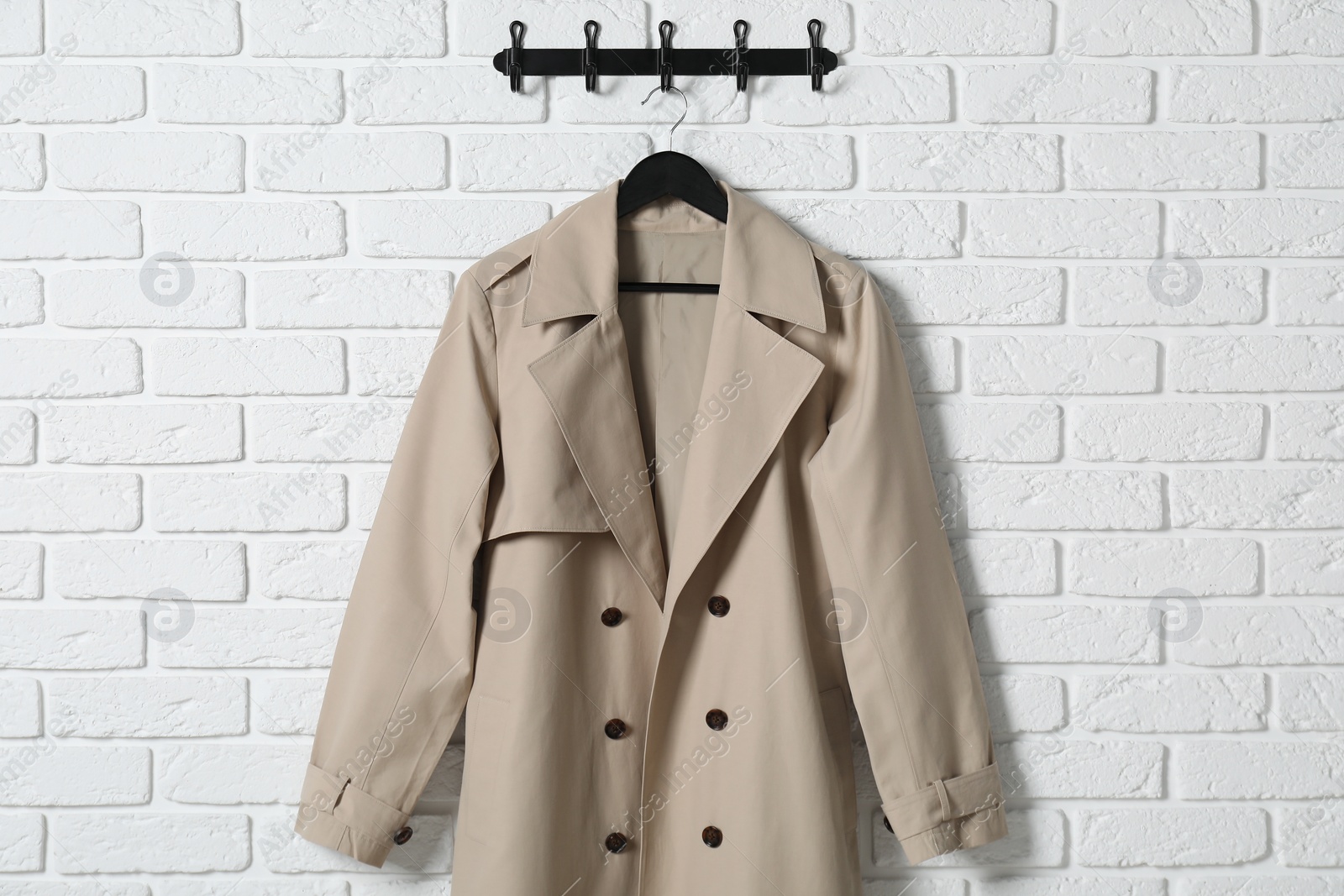 Photo of Hanger with beige coat on white brick wall