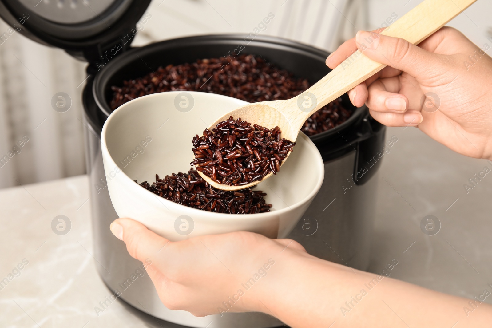 Photo of Woman putting delicious brown rice into bowl from multi cooker, closeup