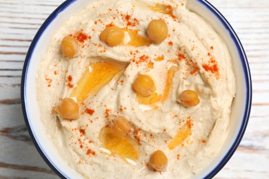 Photo of Bowl of tasty hummus with chickpeas and paprika on white wooden table, top view