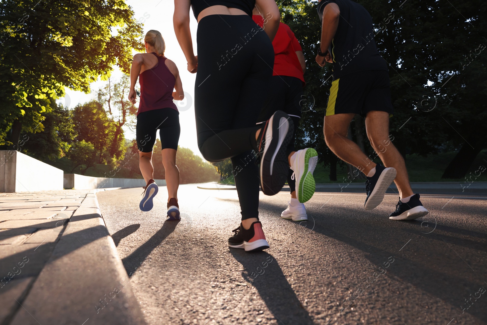 Photo of Group of people running outdoors on sunny day, back view