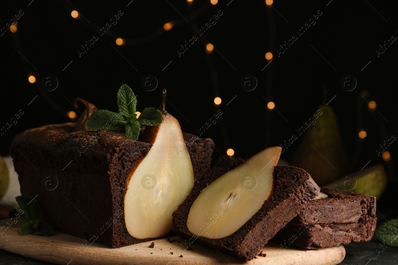 Photo of Tasty pear bread with mint on table against blurred lights. Homemade cake