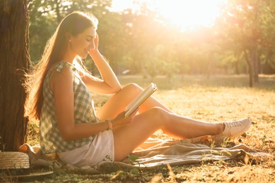 Photo of Young woman reading book on green grass near tree in park