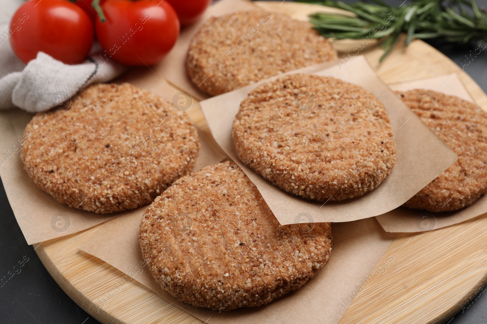 Photo of Raw vegan cutlets with breadcrumbs, tomatoes and rosemary on table, closeup