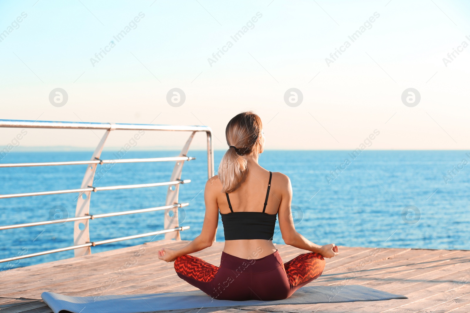 Photo of Young woman doing yoga exercises on pier in morning