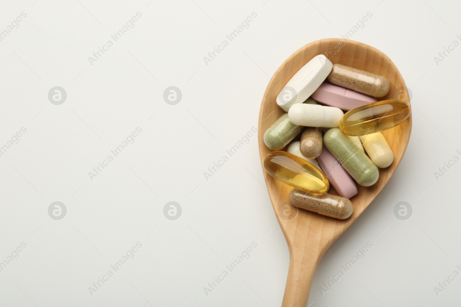 Photo of Different vitamin capsules in spoon on white background, top view. Space for text