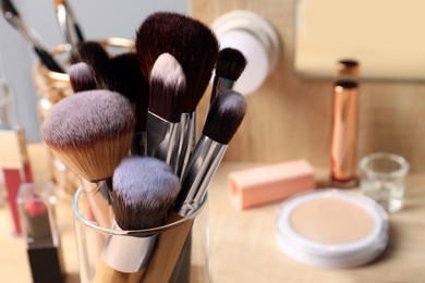 Photo of Set of professional brushes and makeup products near mirror on wooden table, closeup. Space for text
