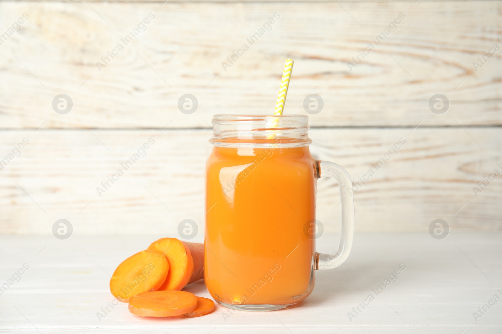 Photo of Freshly made carrot juice in mason jar on white wooden table