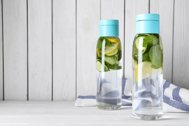 Bottles of refreshing water with cucumber, lemon and mint on white wooden table, space for text